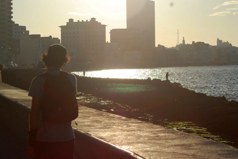 The Havana seafront at sunset: a low orange sun over the water, the sea wall and weathered buildings in silhouette.